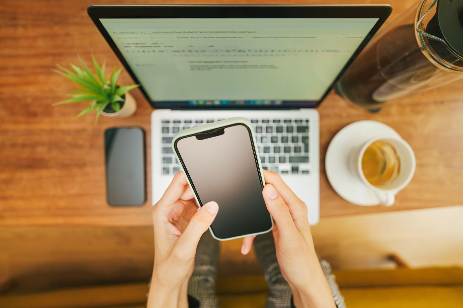Hands holding a phone above an open laptop and a cup of coffee, ready to read a cruise deals newsletter