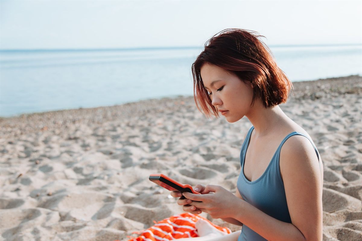 A woman sitting on a sandy beach reading her phone
