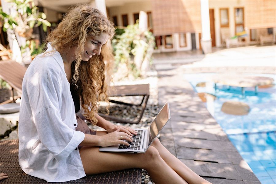 A smiling woman using a laptop beside a hotel pool