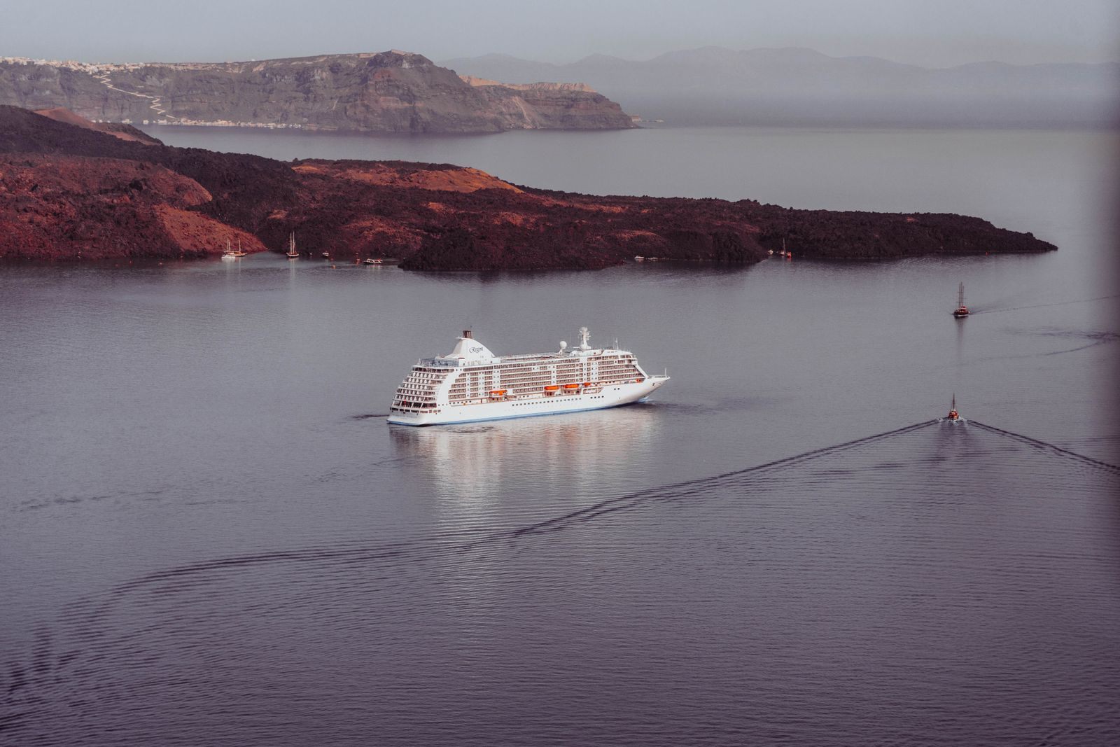 Aerial view of a cruise ship sailing past the volcanic islands of Santorini