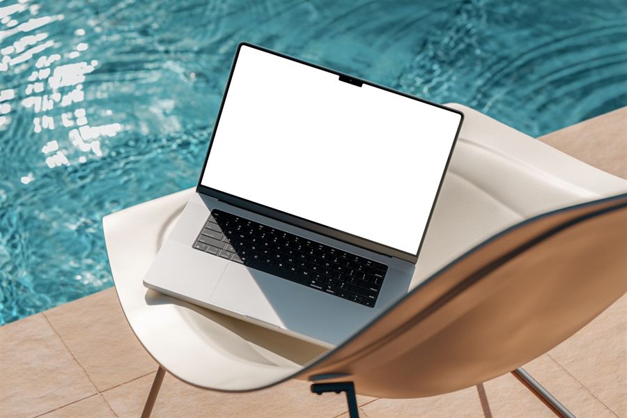 A laptop with a blank screen on a lounge chair beside a swimming pool