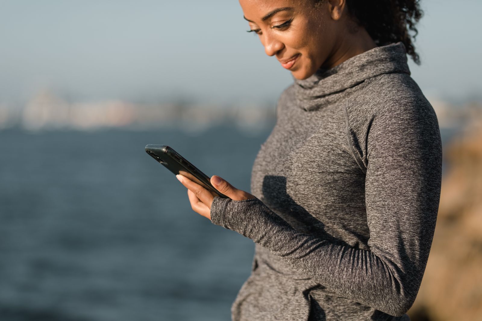 A woman checking her phone beside the sea, the kind of quick cruise newsletter sign up that takes a minute