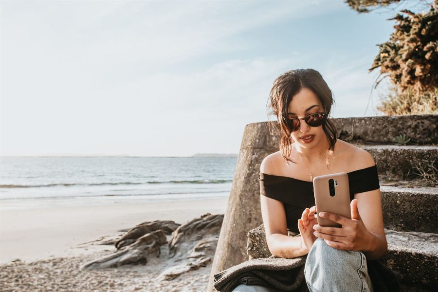 A woman in sunglasses sitting on seaside steps looking at her phone